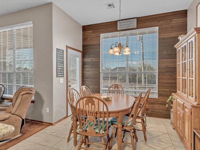 tiled dining space featuring plenty of natural light, a notable chandelier, and wooden walls