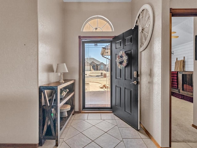 entrance foyer featuring light tile patterned floors, a textured wall, and baseboards