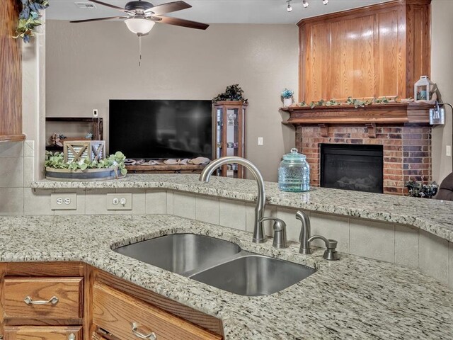 kitchen featuring a ceiling fan, open floor plan, light stone countertops, a fireplace, and a sink