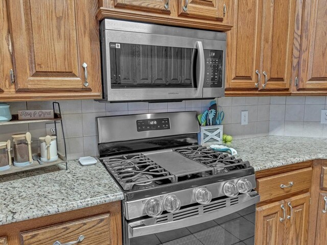 kitchen with stainless steel appliances, brown cabinetry, light stone counters, and tasteful backsplash