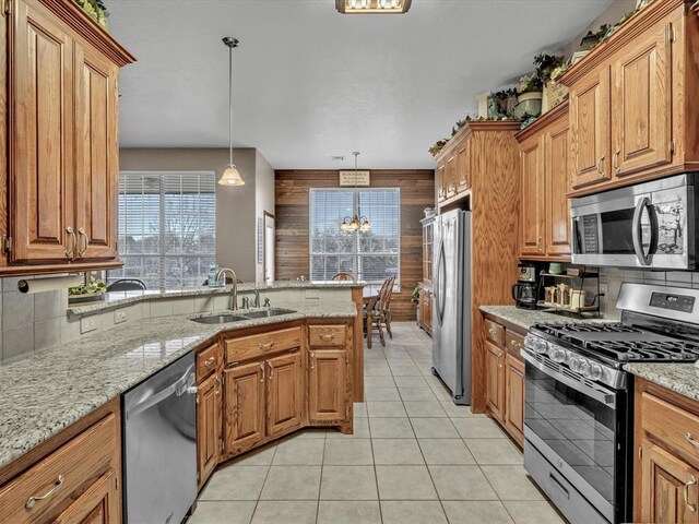 kitchen featuring tasteful backsplash, appliances with stainless steel finishes, a peninsula, wood walls, and a sink