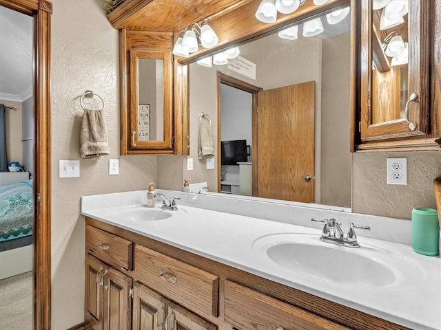 ensuite bathroom featuring a textured wall, ornamental molding, a sink, and connected bathroom