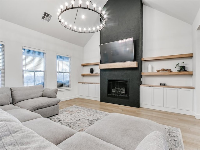 living room featuring lofted ceiling, a fireplace, an inviting chandelier, and light wood-type flooring