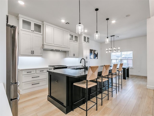 kitchen featuring sink, stainless steel appliances, an island with sink, white cabinets, and decorative light fixtures