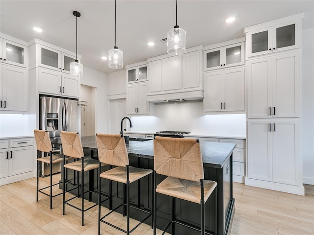 kitchen with a kitchen island with sink, decorative light fixtures, white cabinets, and light wood-type flooring