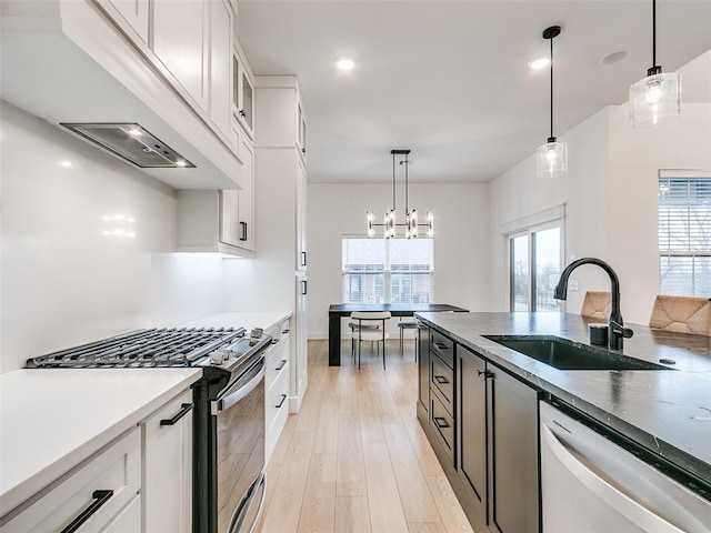 kitchen featuring sink, custom exhaust hood, white cabinetry, hanging light fixtures, and appliances with stainless steel finishes