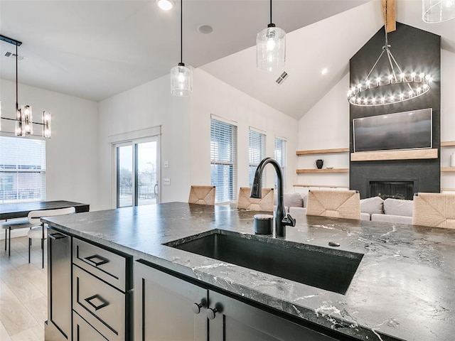 kitchen featuring pendant lighting, sink, light hardwood / wood-style flooring, dark stone countertops, and a large fireplace