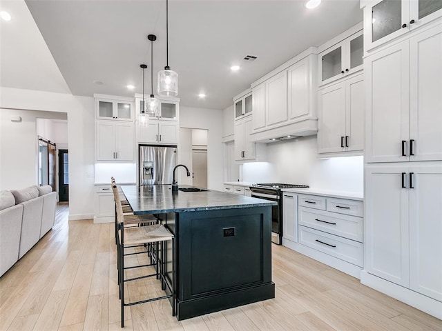 kitchen featuring sink, hanging light fixtures, stainless steel appliances, a center island with sink, and a barn door