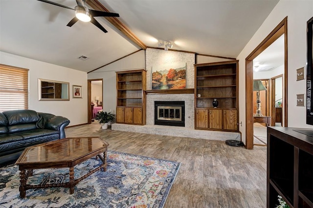 living room with hardwood / wood-style floors, lofted ceiling with beams, ceiling fan, a brick fireplace, and built in shelves