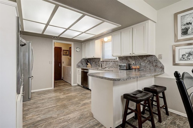 kitchen featuring a breakfast bar area, white cabinets, independent washer and dryer, and kitchen peninsula