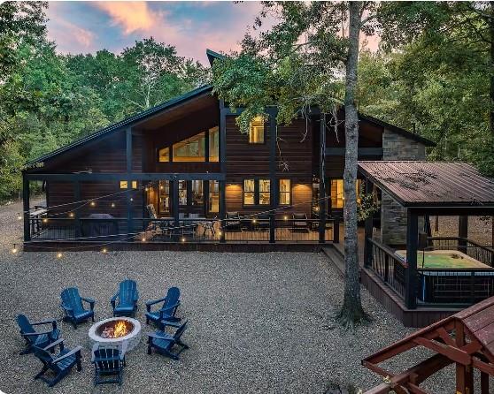 back house at dusk with a jacuzzi, a patio area, and a fire pit