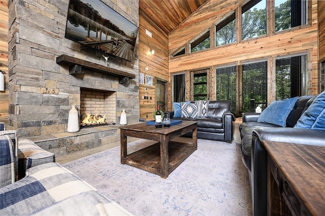 living room with plenty of natural light, an outdoor stone fireplace, wooden ceiling, and wood walls