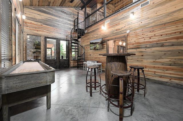 bar with concrete flooring, high vaulted ceiling, wood walls, stairway, and a bar