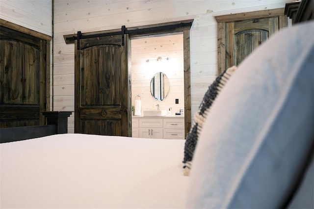 bedroom with a sink, wooden walls, ensuite bath, and a barn door