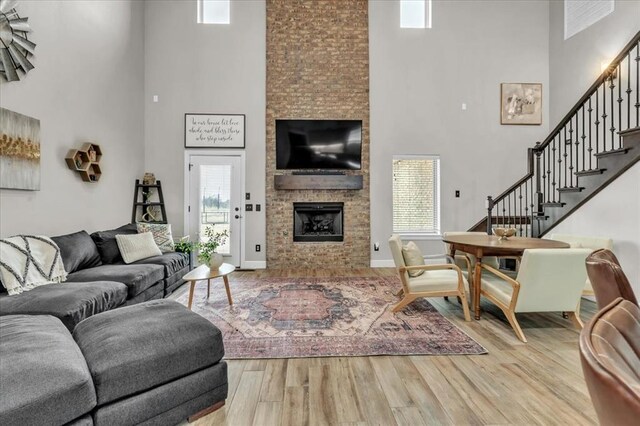 living room featuring a towering ceiling, a fireplace, a healthy amount of sunlight, and light wood-type flooring