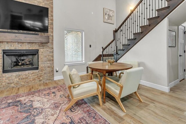 dining space featuring a brick fireplace, a towering ceiling, and light hardwood / wood-style floors