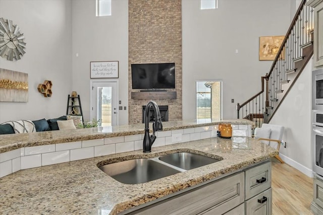 kitchen with sink, light stone counters, a fireplace, and light hardwood / wood-style floors