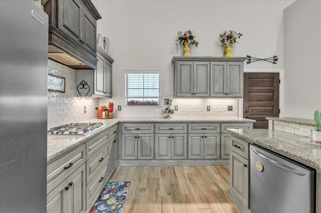 kitchen featuring appliances with stainless steel finishes, gray cabinetry, light stone countertops, decorative backsplash, and light wood-type flooring