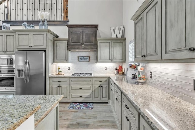 kitchen with appliances with stainless steel finishes, light stone counters, light hardwood / wood-style floors, and decorative backsplash