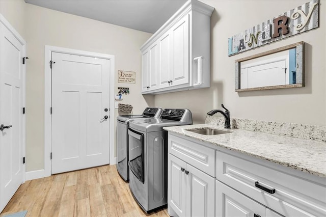 clothes washing area with sink, cabinets, washer and dryer, and light wood-type flooring