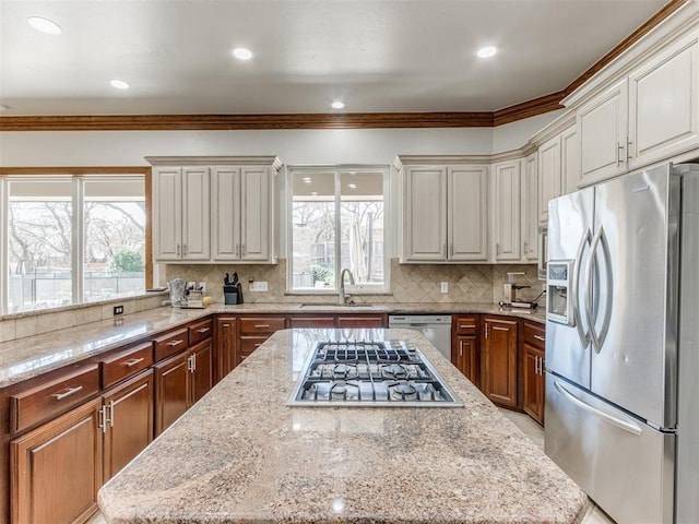 kitchen featuring sink, crown molding, stainless steel appliances, light stone counters, and a kitchen island