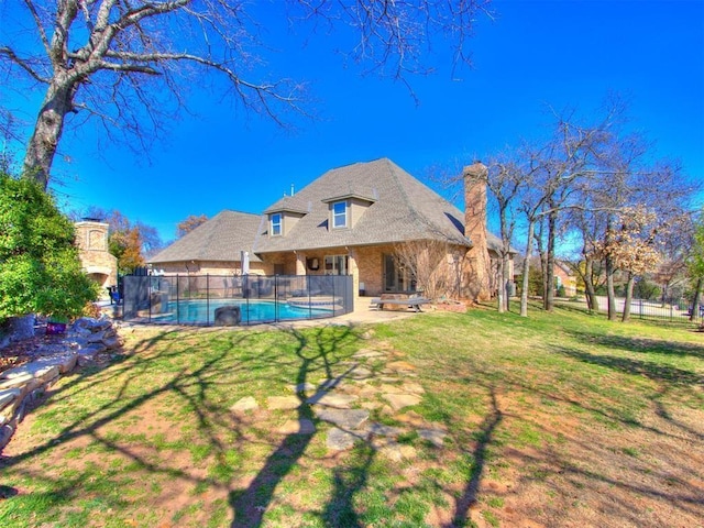 back of property featuring exterior fireplace, a yard, a fenced in pool, and a patio