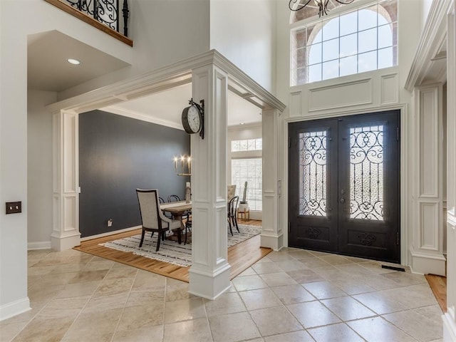 entrance foyer with ornate columns, a towering ceiling, a chandelier, ornamental molding, and french doors