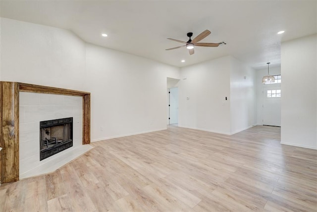 unfurnished living room with ceiling fan, a tiled fireplace, and light wood-type flooring