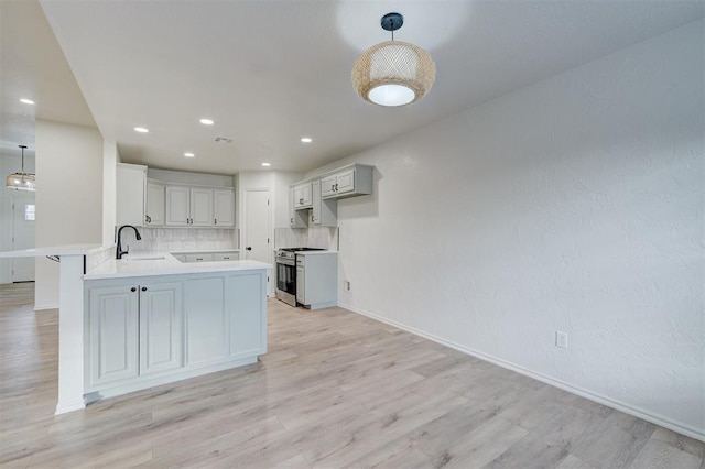 kitchen with sink, light hardwood / wood-style flooring, stainless steel gas range, decorative backsplash, and kitchen peninsula