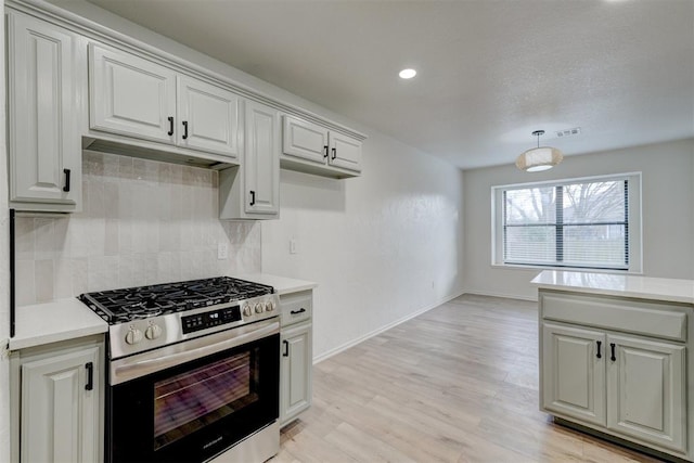 kitchen featuring gas range, pendant lighting, light hardwood / wood-style floors, and backsplash