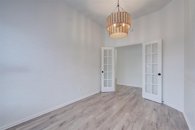 unfurnished room featuring a notable chandelier, a towering ceiling, light hardwood / wood-style floors, and french doors