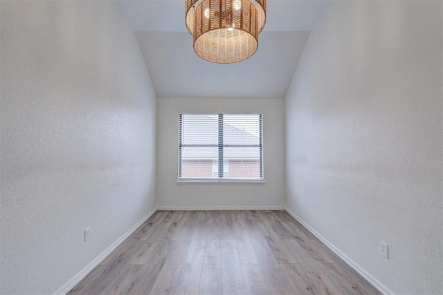 empty room with a notable chandelier, light hardwood / wood-style flooring, and vaulted ceiling