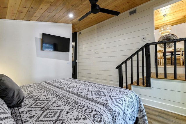 bedroom with wood-type flooring, wooden walls, ceiling fan with notable chandelier, and wooden ceiling