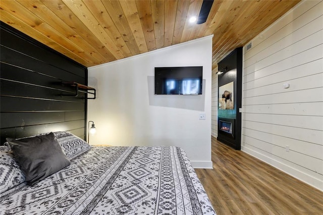 bedroom with vaulted ceiling, wood walls, wood-type flooring, ornamental molding, and wooden ceiling