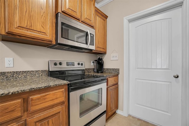 kitchen with crown molding, stainless steel appliances, light tile patterned floors, and dark stone counters