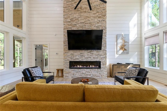 living room with hardwood / wood-style flooring, wood walls, a stone fireplace, and a high ceiling