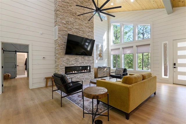 living room featuring a stone fireplace, wood ceiling, high vaulted ceiling, light wood-type flooring, and a barn door