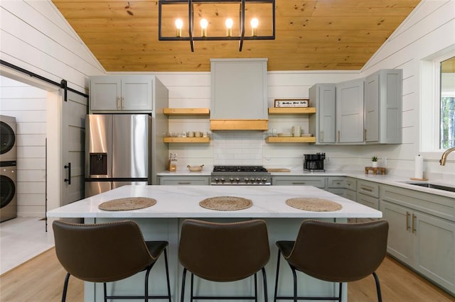 kitchen with lofted ceiling, stainless steel fridge, stacked washer and clothes dryer, and a barn door