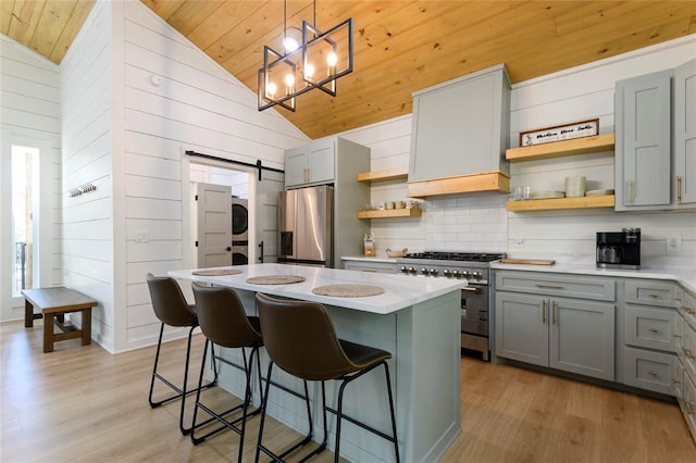 kitchen with stacked washing maching and dryer, appliances with stainless steel finishes, pendant lighting, lofted ceiling, and a barn door