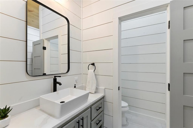 bathroom with vanity, wooden walls, and toilet