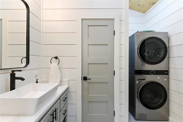 washroom with stacked washer and dryer, sink, and wooden walls