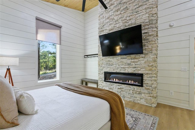 bedroom with wooden walls, a fireplace, vaulted ceiling, wooden ceiling, and light wood-type flooring