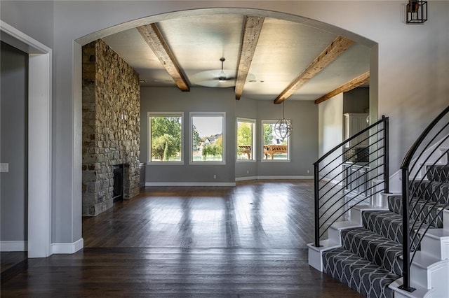 living room featuring beamed ceiling, a stone fireplace, dark wood-type flooring, and ceiling fan