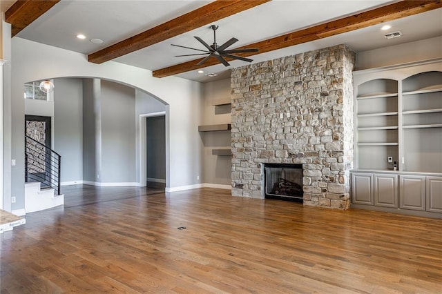 unfurnished living room featuring ceiling fan, hardwood / wood-style floors, beam ceiling, a fireplace, and built in shelves