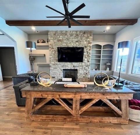 living room with beamed ceiling, wood-type flooring, ceiling fan, and a fireplace