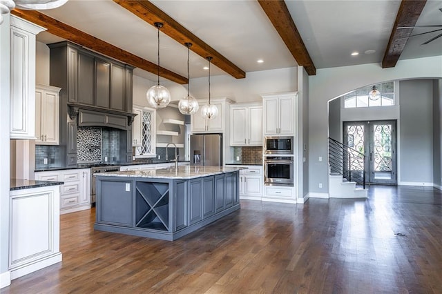 kitchen with appliances with stainless steel finishes, white cabinetry, backsplash, hanging light fixtures, and a kitchen island with sink