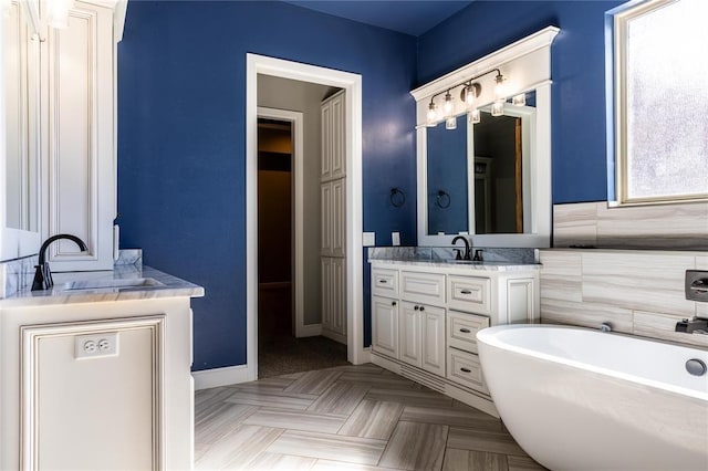 bathroom featuring parquet flooring, tile walls, vanity, a healthy amount of sunlight, and a bath