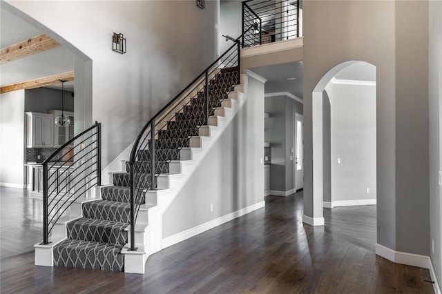 foyer entrance with crown molding, beamed ceiling, dark wood-type flooring, and a high ceiling