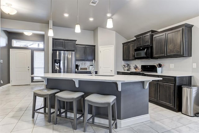 kitchen featuring tasteful backsplash, decorative light fixtures, a kitchen island with sink, and black appliances