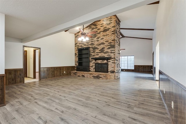 unfurnished living room with ceiling fan, a brick fireplace, a textured ceiling, and light hardwood / wood-style floors